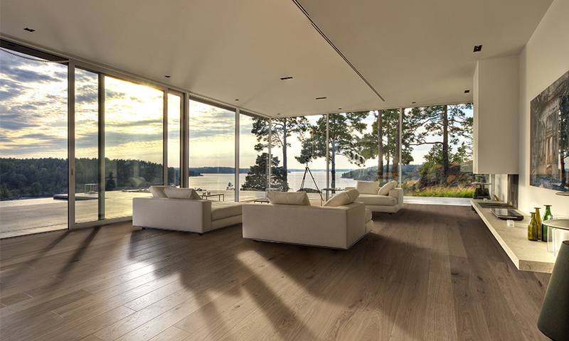 Moderne stue med beige sofaer, mørkt tregulv og store vinduer mot innsjø og skog