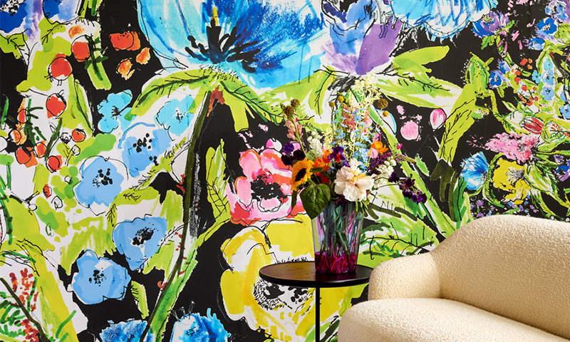 Interiørhjørne med fargerikt blomsterprint-tapet, kremstol og bord med fargerik vase