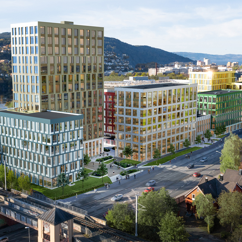 Flerfargede kontorbygg (grønt, gult, rødt, blått) ved vei med trafikk og ås i bakgrunnen