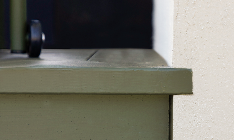 Grønnmalt vinduskarm mot hvit vegg, med et lite svart hjul på venstre side.