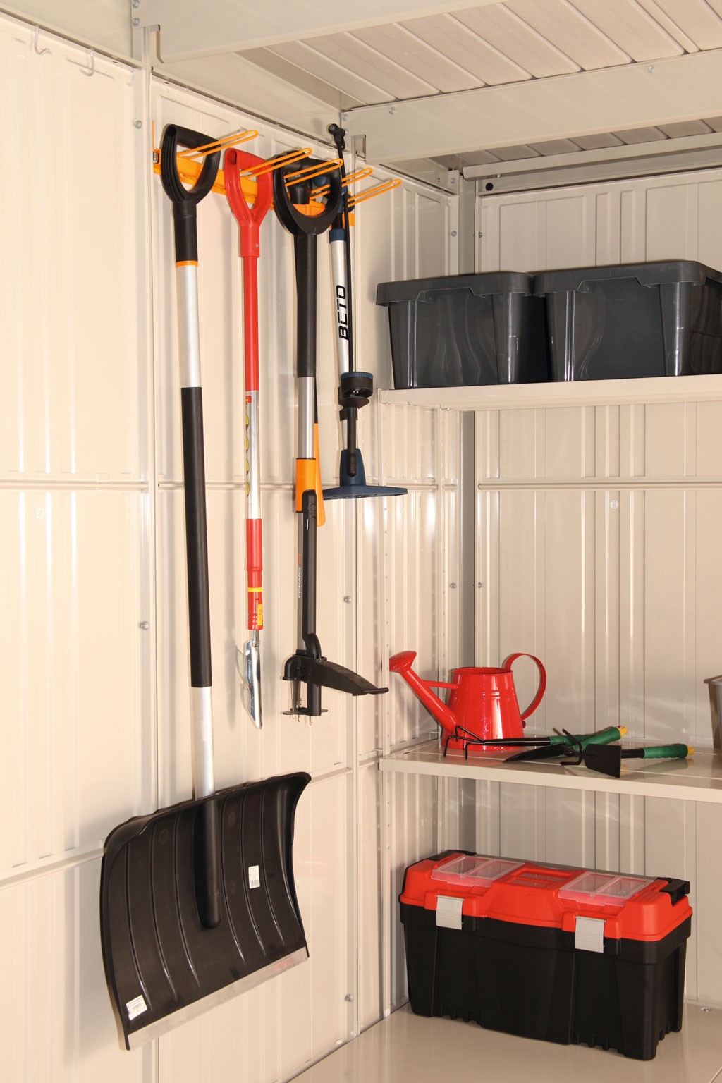 Hvit metallbod med hengende spade, snøskuffe, rød vannkanne og sort-rød verktøykasse