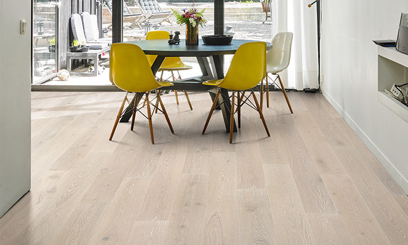 Lyst spisehjørne med rundt svart bord, tre gule og en hvit stol, vase med blomster på lyst tregulv