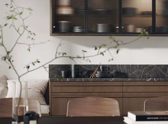 Moderne kjøkken med svart marmorbakvegg, trefronter, glassoverskap og grønne kvister.