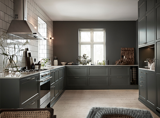 Moderne kjøkken med mørkegrønne skap, hvite fliser, eikegulv, potteplanter og vinduslys