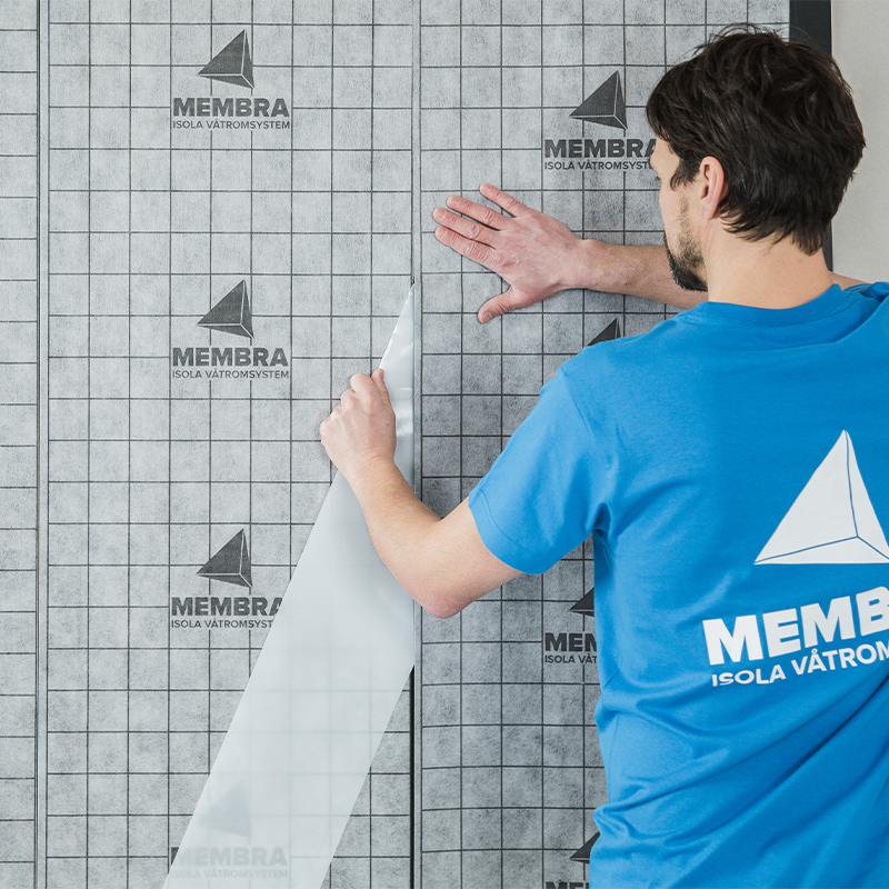 Mann i blå Membra-skjorte fester grå rutet våtromsfolie med Membra-logo på vegg.