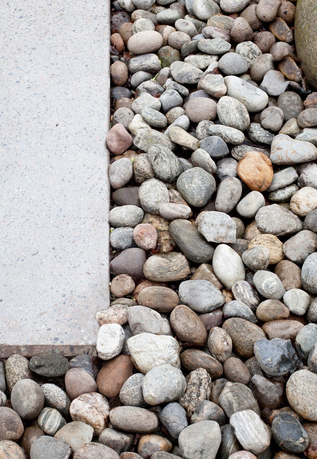 Lys grå betongplate ved siden av blandede elvestein i grå, brune og beige toner.