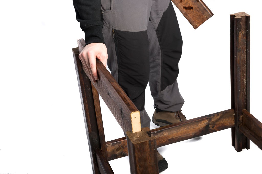 Person i grå/svarte arbeidsklær holder en brun beiset trebordramme på hvit bakgrunn