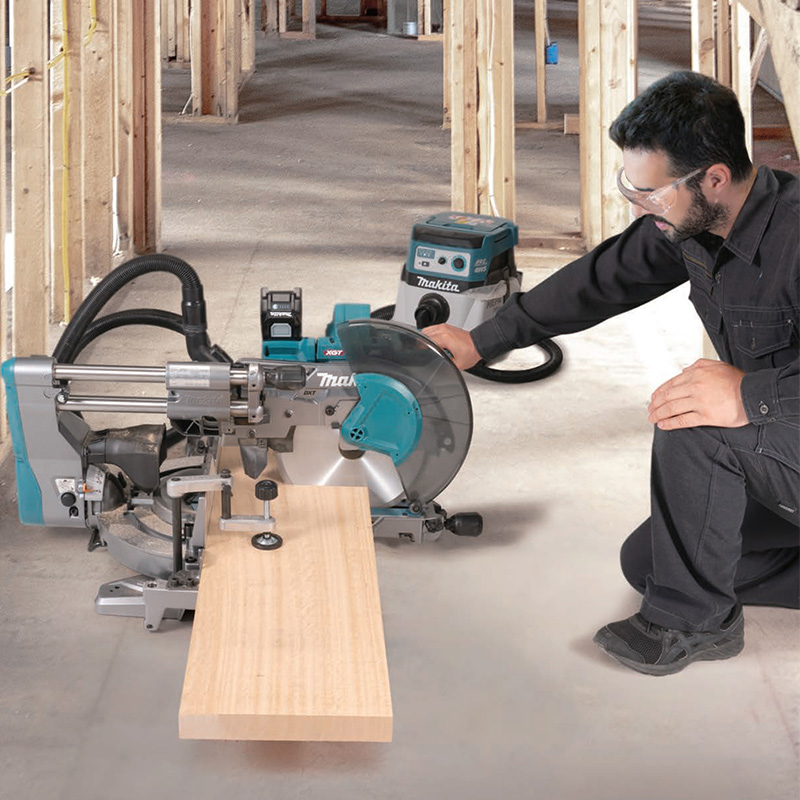 Blå miter-sag kapper lys treplanke på betonggulv i uferdig bindingsverksrom