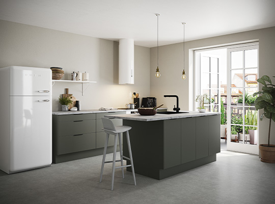 Lyst kjøkken med grønngrå kjøkkenøy, marmortopp, hvitt kjøleskap, hengelamper, vindu med planter.