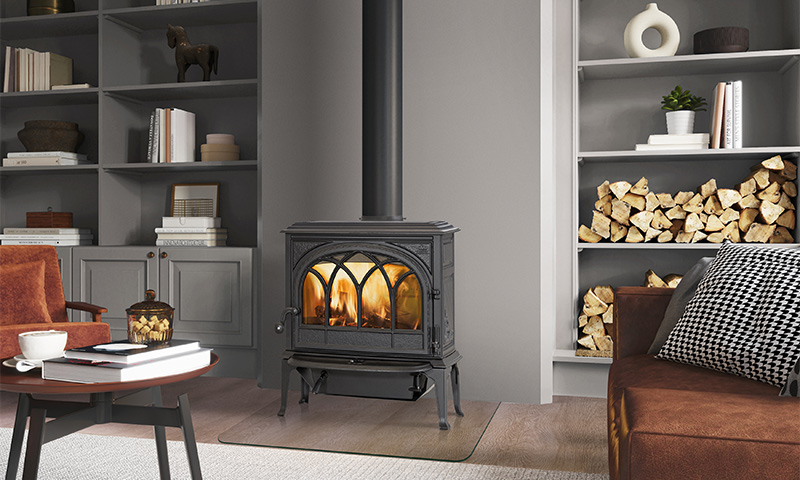 Svart vedovn med flammer, grå bokhyller med ved, brun sofa og trebord