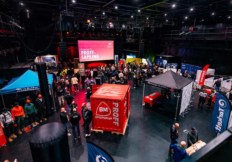 Oversiktsbilde av Byggmakker Proff-samling med mange besøkende, stands og en rød container i en stor hall.