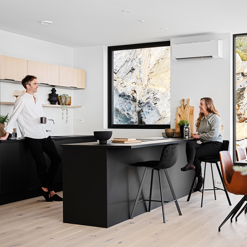 Par som sitter ved kjøkkenet i et lyst som med sorte vinduskarmer