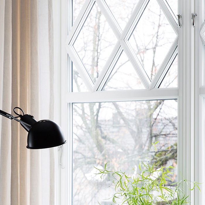 Hvit vindusramme med glassruter i diamantmønster, svart skrivebordslampe og grønn potteplante.