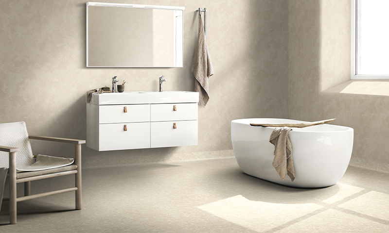 Moderne lyst baderom med beige vegger, hvit dobbel vask m/speil, frittstående badekar og lenestol.