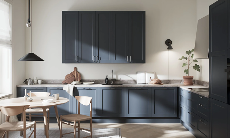 Moderne kjøkken med mørkeblå skap, lys benkeplate, rundt trebord, hengelampe og grønn plante.