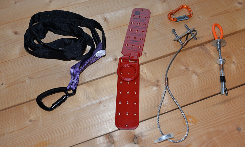 Klatreutstyr: svart slyngeslynge med karabin, rød plate, wirer og bolter på trebord