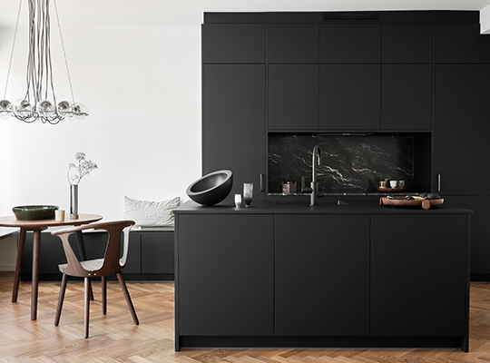 Minimalistisk kjøkken med matte svarte skap, marmorbakvegg, eikegulv, trebord og glasslampe