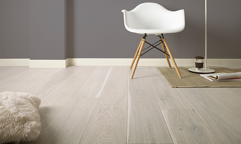 Minimalistisk interiør: lys eikegulv, grå vegg, hvit stol, gulvlampe, teppe med kaffekopp.