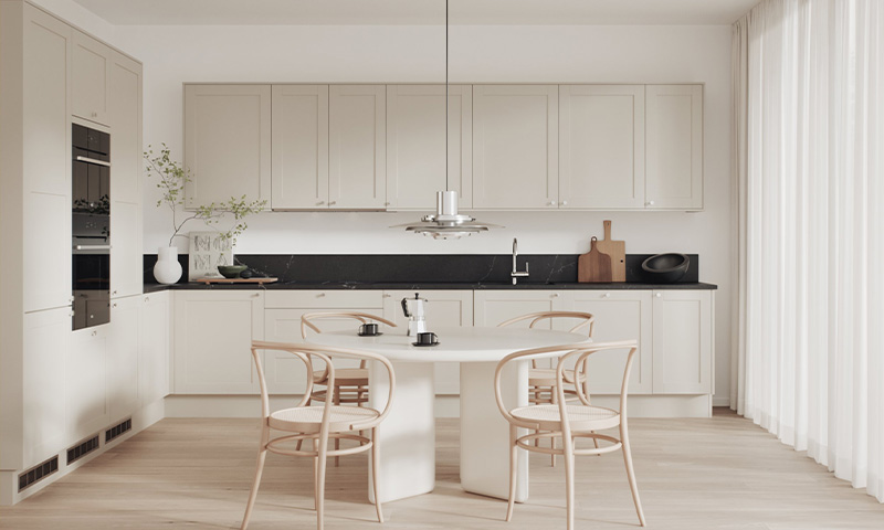 Lyst og luftig kjøkken med beige skap, svart benkeplate, rundt hvitt bord og lyse trestoler.