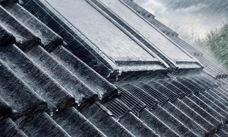 Vinklet nærbilde av mørke grå takstein i kraftig regnvær