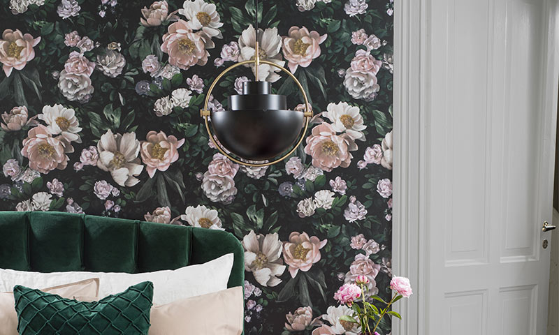 Soverom med mørk blomsterbakgrunn, grønn sengegavl, svart-gull pendel og rosa peoner