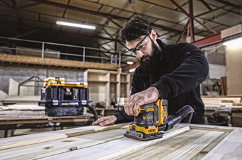 Person pusser treplate med gul-svart el-sander i stort lyst verksted