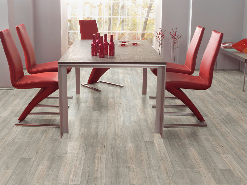 Moderne spisebord i grått med fire røde designerstoler, røde flasker på bordet og stort vindu bak