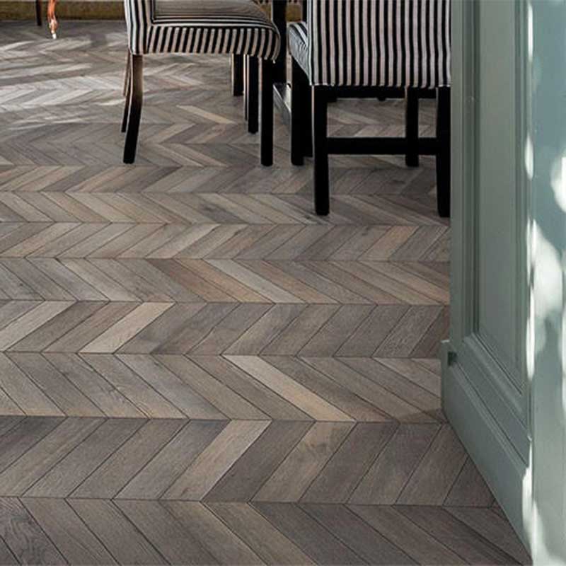 Interiør med gråbeiset fiskebeinsparkett, svarte og hvite stripete stoler og dempet grønn dørkarm