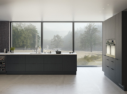 Minimalistisk mørk grå kjøkkenøy foran stort panoramavindu med disig skogutsikt