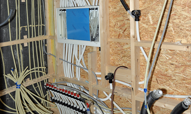 Åpen veggkonstruksjon med hvite rør, blå koblingsboks og røde ventiler.