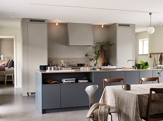 Moderne åpent kjøkken med grå skap, kjøkkenøy, spisebord med stoler og grønne planter. Lyst og minimalistisk interiør.
