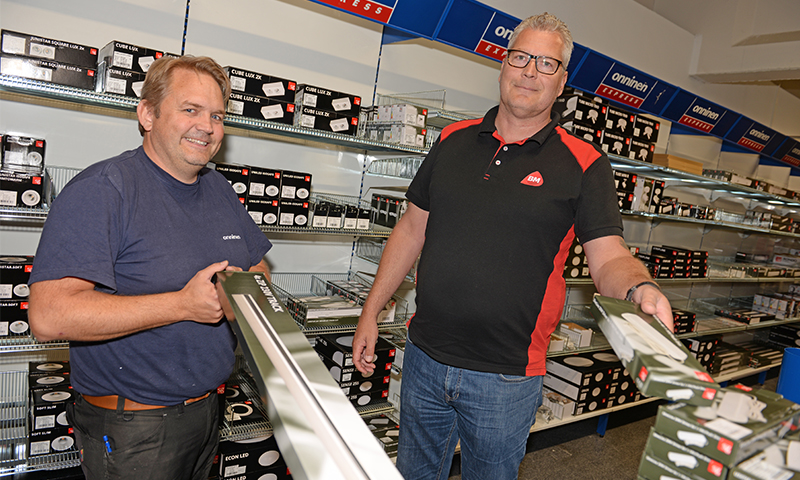 To menn i elektrobutikk omgitt av hyller med LED-lysarmaturer, holder lange hvite LED-lister.