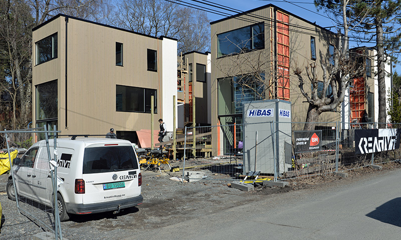 Moderne beige funkishus under oppføring med byggeplassgjerde, varebil og HiBAS-do.