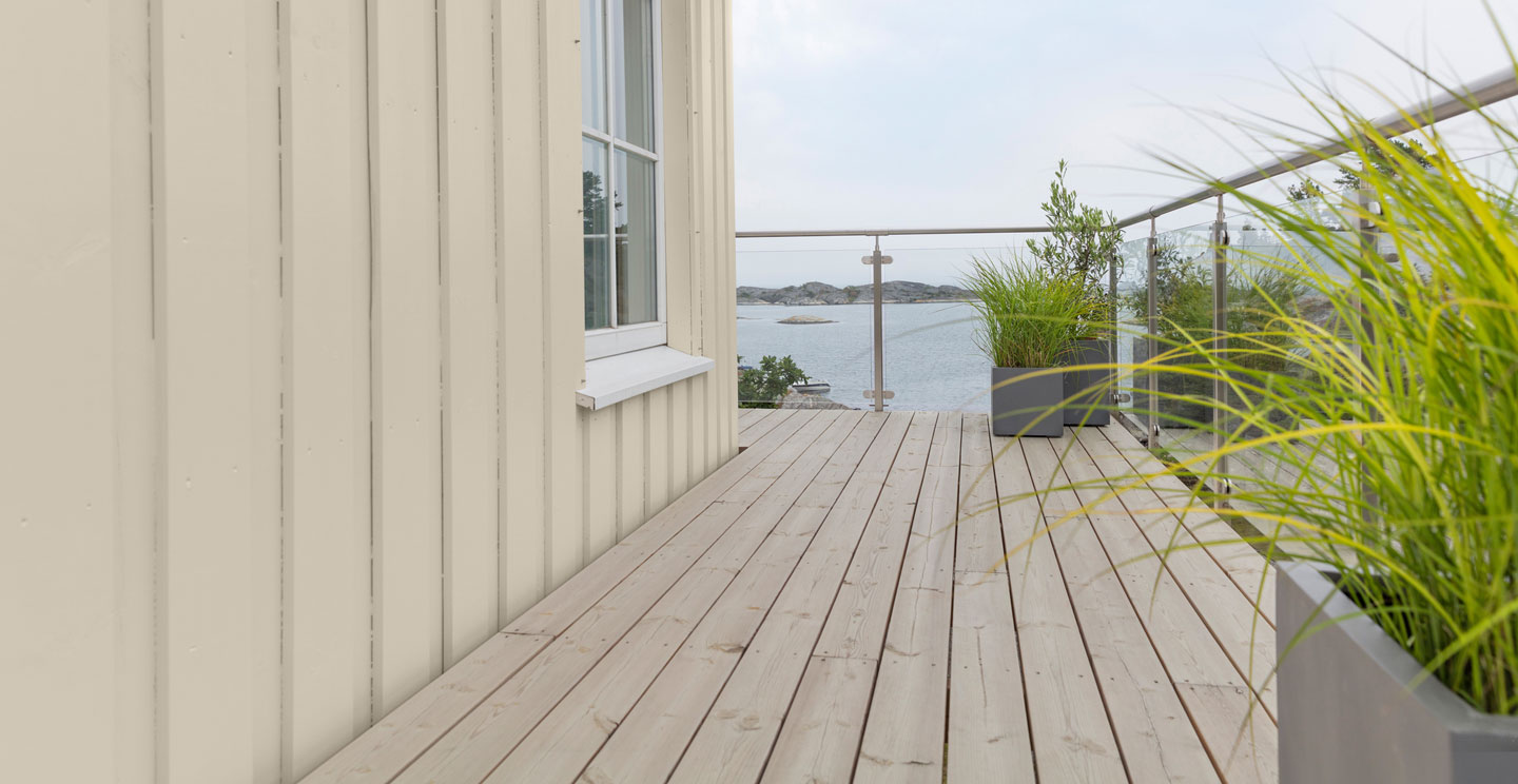 Lyst tredekke med grå rekkverk og grønne planter, utsikt mot rolig sjøøylandskap
