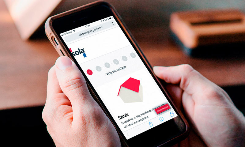 Hender holder smarttelefon med Isola takberegning: rød-beige saltak-ikon på hvit skjerm over trebord