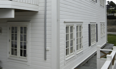 Hvit trevilla med panelet fasade, flere hvite sprossevinduer og lav veranda i rolig boligområde