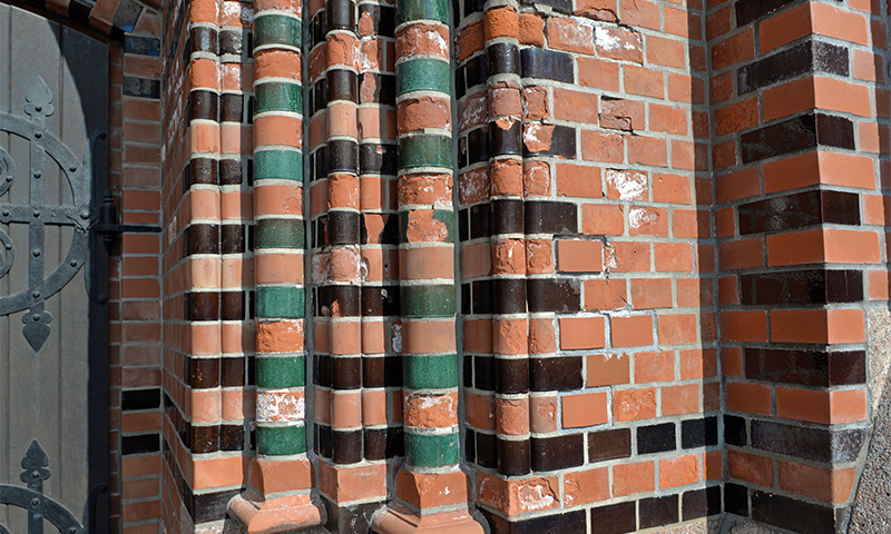 Nærbilde av rødoransje mursteinsvegger med glaserte grønne og svarte søyler ved port