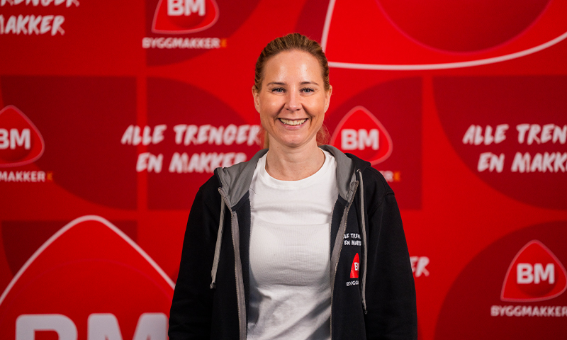 Person i hvit T-skjorte og svart hettegenser med BM-logo foran rød reklamevegg