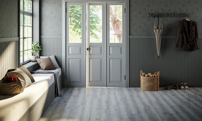 Lys grå entré med vindusbenk og puter, kurv med ved, hengende paraply, dører mot hage.
