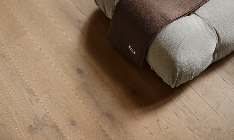 Lys eikegulv med en myk grå gulvpute og et brunt pledd.