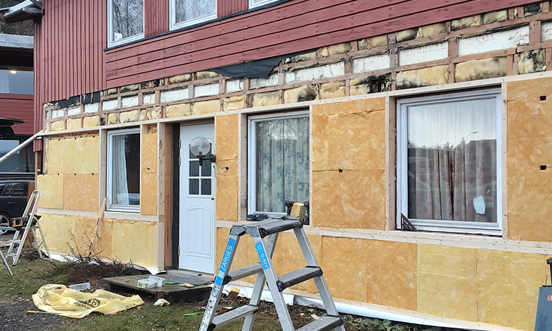 Rødt hus under renovering med gule isolasjonsplater, hvit dør og stige.