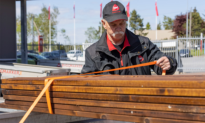 Ansatt strammer oransje stroppebånd rundt brune treplanker utenfor byggevarebutikk