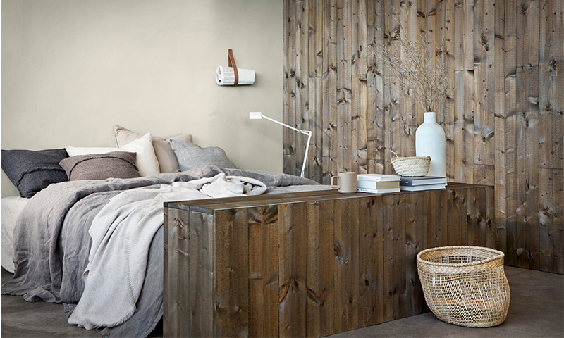 Lyst soverom med stor seng, grått sengetøy og trefinerte veggpaneler, kurv og vaser.