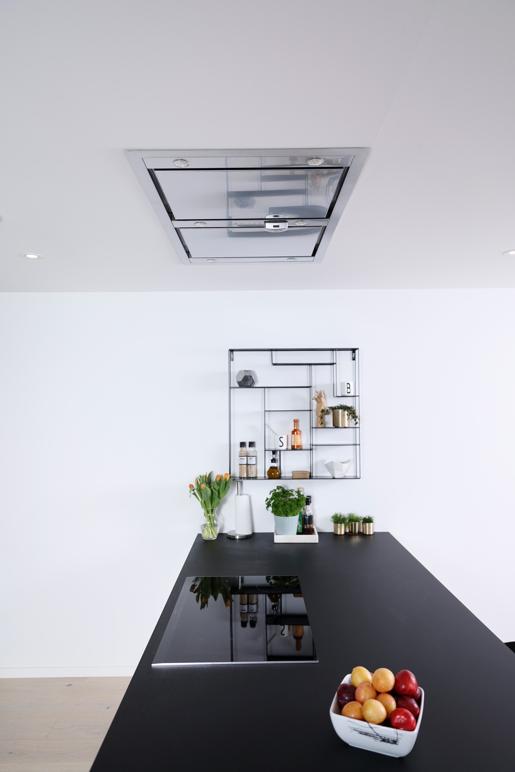 Moderne kjøkkenøy med svart benkeplate, glasskoketopp, metallhylle, frukt og urter.