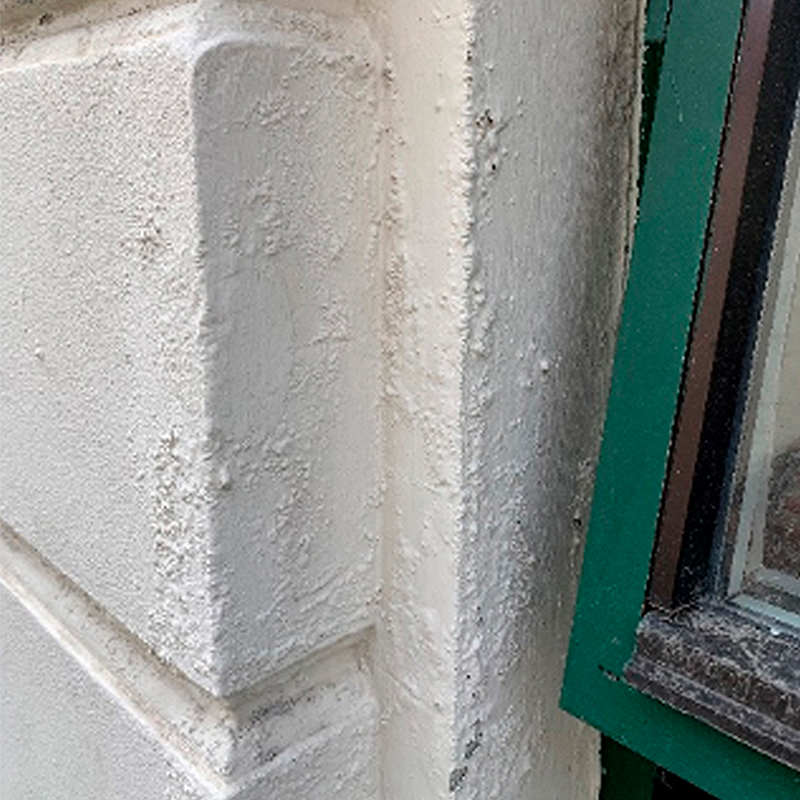 Nærbilde av hvitt, ru pussfasadehjørne og grønn vinduskarm med brune lister.