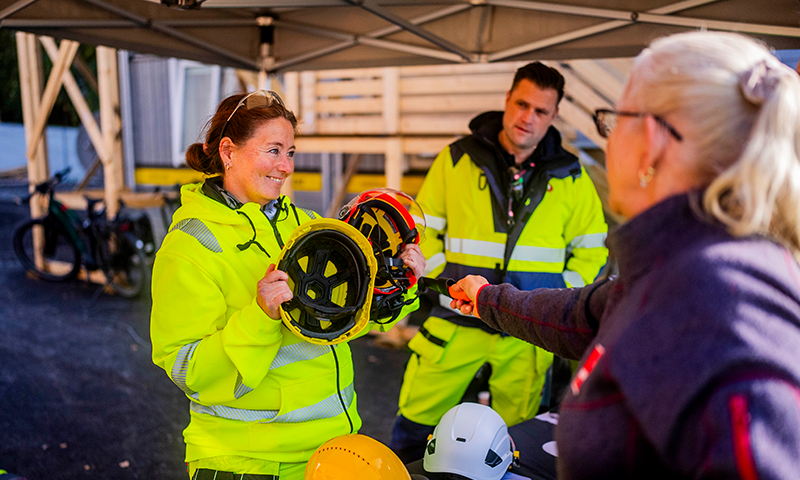Person i neongul arbeidsdrakt viser gule og røde hjelmer på byggeplass mens annen peker.