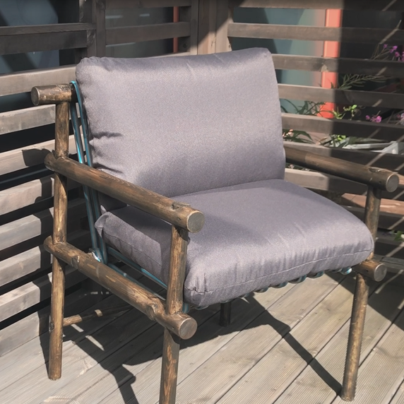 Trestol med grå puter på solfylt treterrasse foran gitterrekkverk.