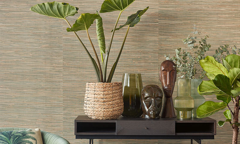 Mørkt trebord med frodige grønne planter i kurv, flere grønne glassvaser og treskulptur