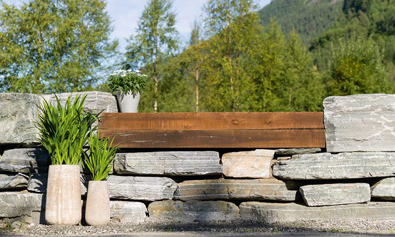 Steinbenk med treplate, to beige potter med grønne planter og hvit blomsterpotte, skogbakgrunn.