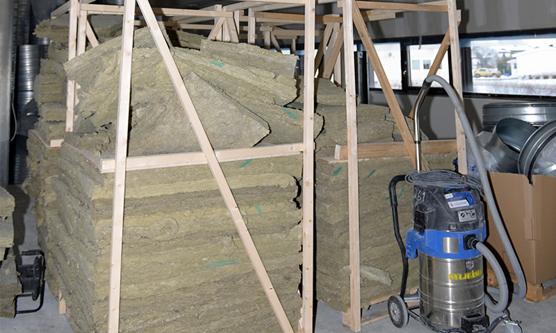 Stabel av grønne isolasjonsplater i trestativ ved blå-sølv industristøvsuger i byggeinteriør